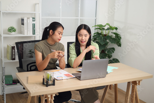 Portrait of Two Asian businesswoman are working together at a desk, discussing documents while looking at a laptop screen. Business ideas and strategies