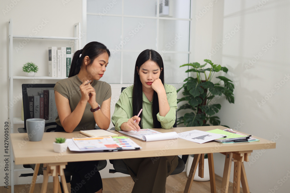 Portrait of Two female colleagues are sitting together at desk, reviewing documents and discussing work in the office.