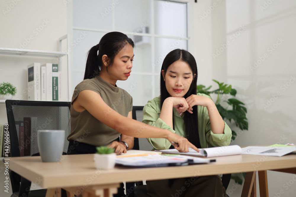 Portrait of Two female colleagues are sitting together at desk, reviewing documents and discussing work in the office.