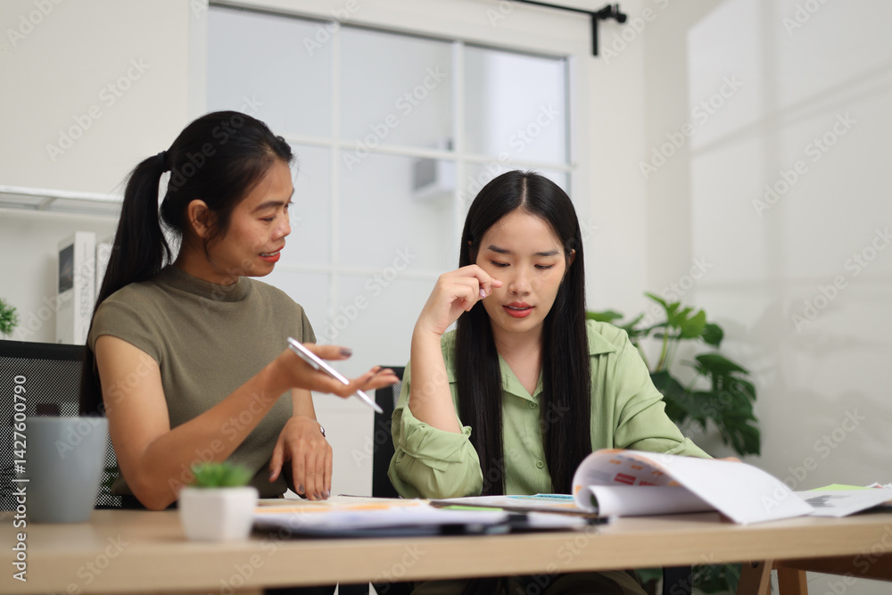 Portrait of Two female colleagues are sitting together at desk, reviewing documents and discussing work in the office.