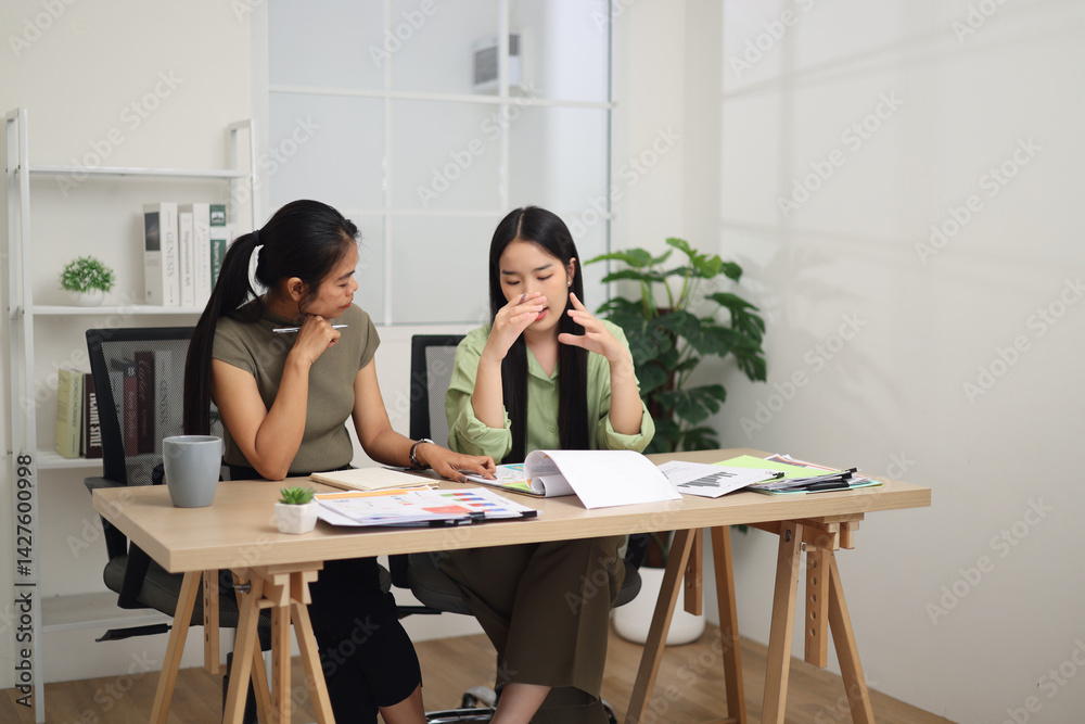 Portrait of Two female colleagues are sitting together at desk, reviewing documents and discussing work in the office.