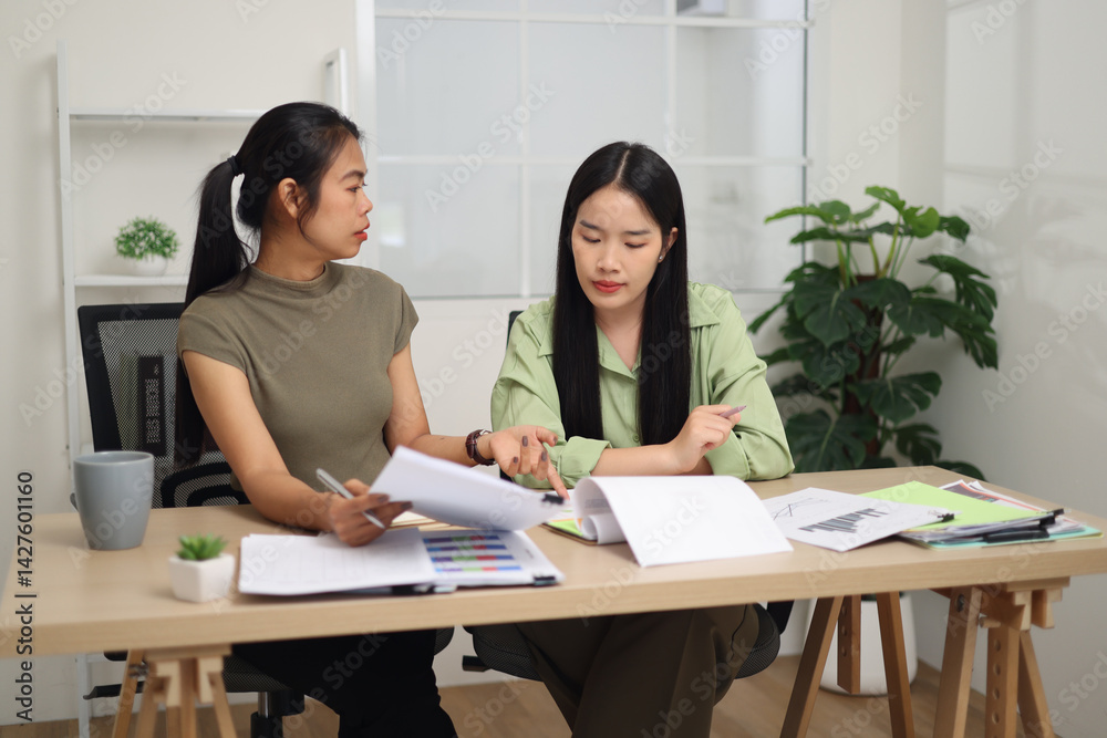 Portrait of Two female colleagues are sitting together at desk, reviewing documents and discussing work in the office.