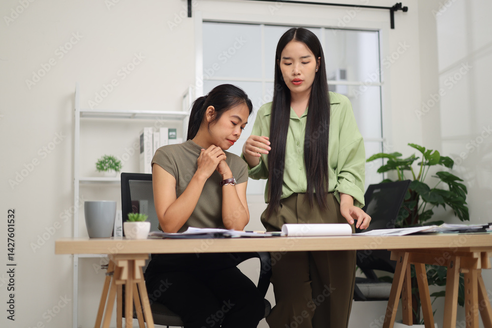 Low angle view shot, Two female colleagues are working together in an office. One stands explaining the work, while the other sits and listens with interest.