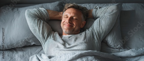 Relaxed middle aged European in bed. Smiling relaxing. Lying comfortably on grey bedding. Top view. enjoys morning. Happy person. Comfortable lifestyle. Home atmosphere. Morning vibes. Good