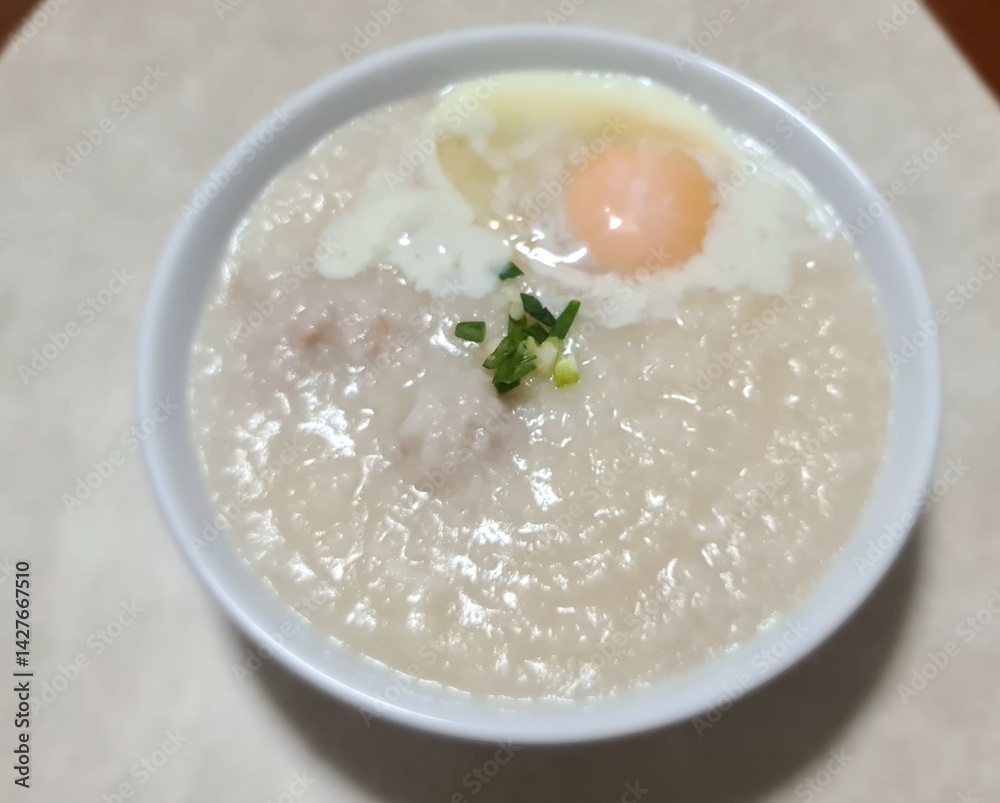 pork and rice porridge with soft boiled egg in white bowl on table pork and rice porridge with soft boiled egg in white bowl on table