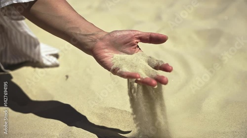 An extreme close-up of a woman's hand as dry sand slips through her fingers and scatters in the wind - a powerful slow motion visualization of land desertification