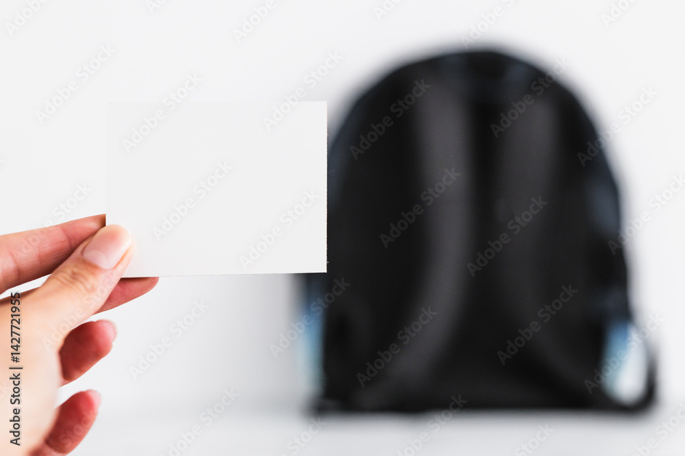 hand holding blank message label in front of backpack, concept of backpacking, travelling or going to school