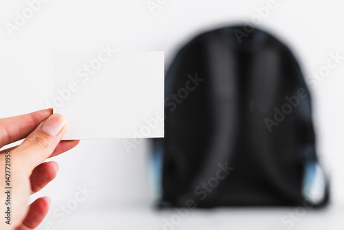 Obraz na płótnie hand holding blank message label in front of backpack, concept of backpacking, travelling or going to school w salonie