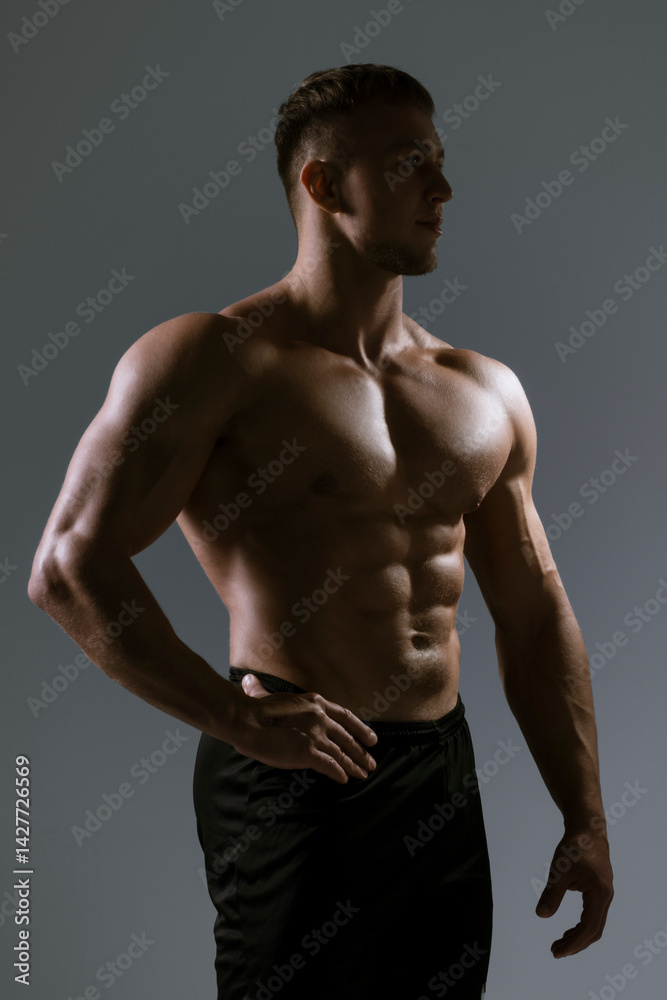 Fototapeta premium A Muscular Male Model captured in a Profile Pose with Dramatic HighContrast Lighting
