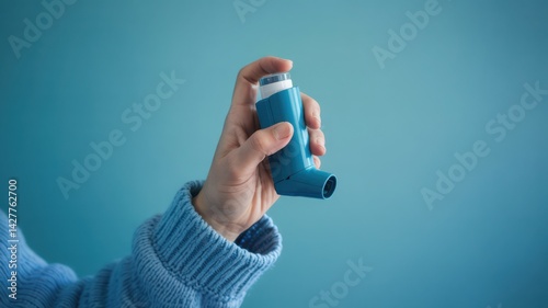 Hand Using Asthma Inhaler on Blue Background for Respiratory Health Awareness and Daily Treatment