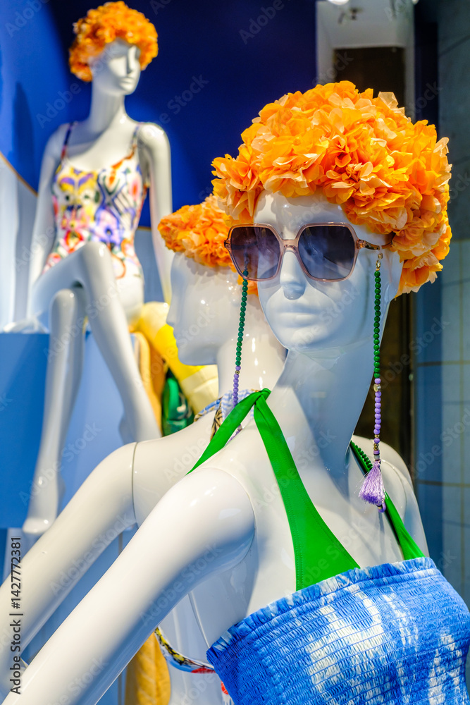 Mannequins displaying vibrant summer swimwear at a retail shop window, showcasing bold colors and accessories for the sunny season