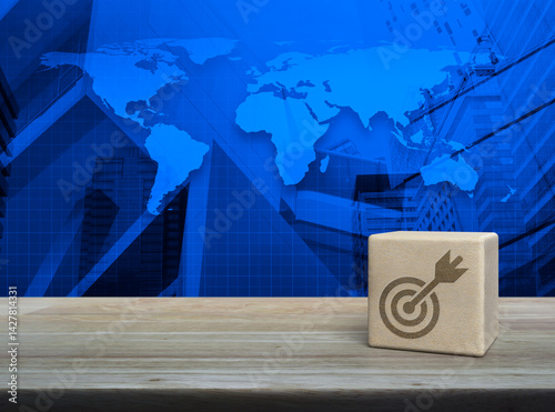 Fototapeta Naklejka Na Ścianę i Meble -  Target with dart icon on wood block cube on wooden table over world map, modern office city tower and skyscraper, Business success concept, Elements of this image furnished by NASA