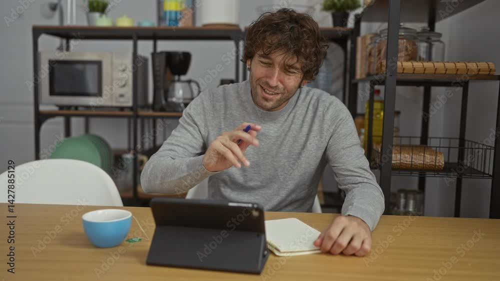 Young man writing notes with tablet in modern office with shelves and coffee maker. Young man writing notes with tablet in modern office with shelves and coffee maker.