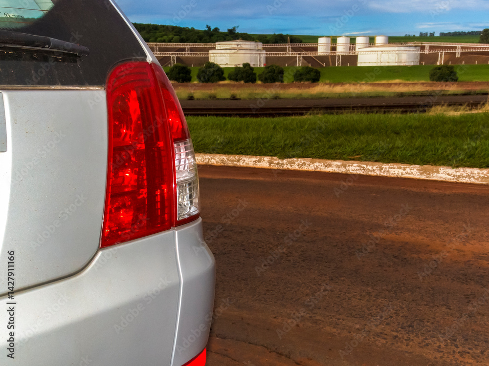 Car on red dirt road with ethanol storage tanks in background, Brazil. Illustrates biofuel transport & infrastructure