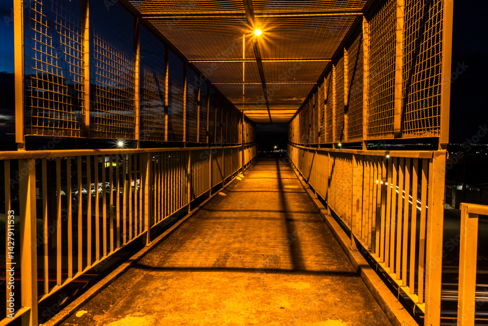Night view of a pedestrian bridge with yellow lighting. Dramatic urban scene, suitable for city infrastructure, safety, or design themes. Striking contrast