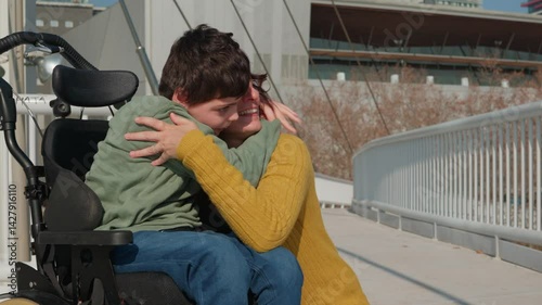 Mother embracing disabled son in wheelchair on bridge photo