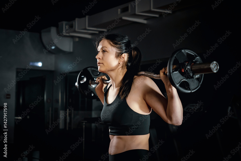 Side view of athletic woman in sexy sport outfit lifting barbell at gym room background. Attractive young sport Muscular woman working out in gym. Crossfit training. lifting barbell