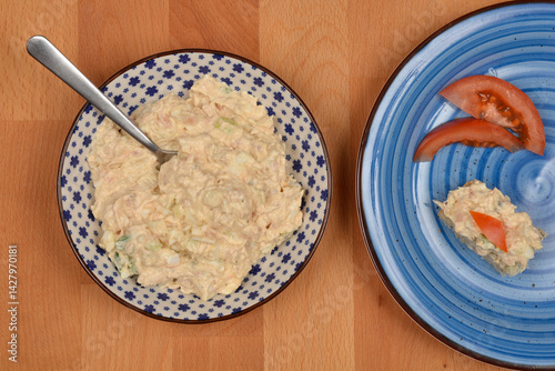 Obraz na płótnie A small canape with tuna, cream cheese, egg, caper, onion, and mustard spread and tomato sits on a blue plate next to a bowl of the spread with a spoon w salonie
