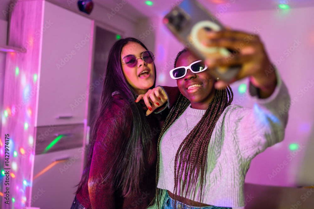 Two cheerful teenagers taking a selfie with smartphone at home party