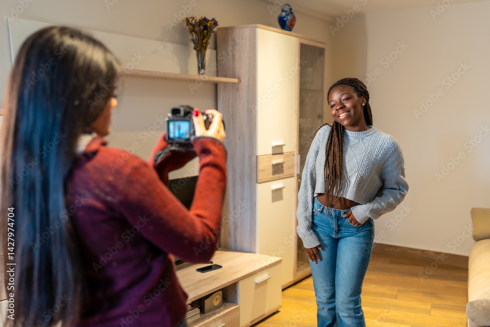 Young photographer taking pictures of her friend posing at home