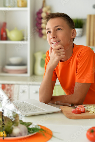 Obraz na płótnie Teen boy thinking while working on laptop in kitchen w salonie