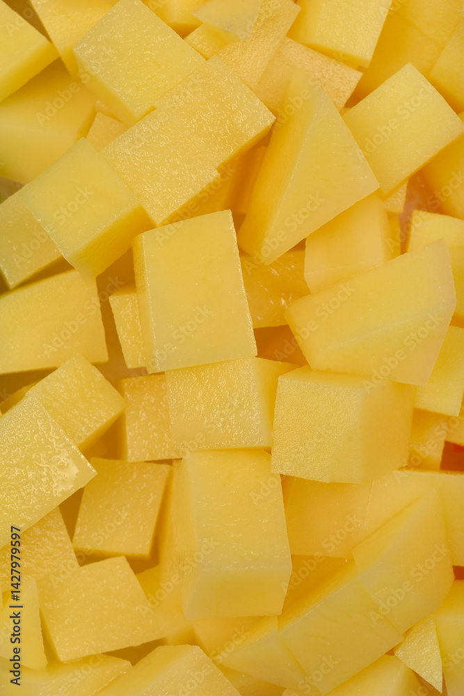 A close-up, top-down shot shows a jumbled pile of raw, light yellow diced potatoes