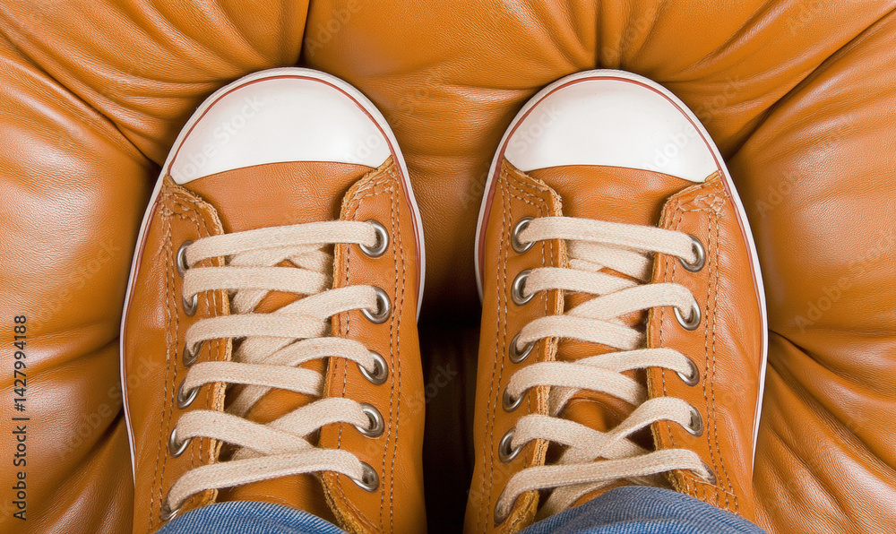 Stylish Casual Footwear on a Comfortable Brown Leather Surface with Tied Shoelaces and Vibrant Orange Background for Fashion and Lifestyle Imagery