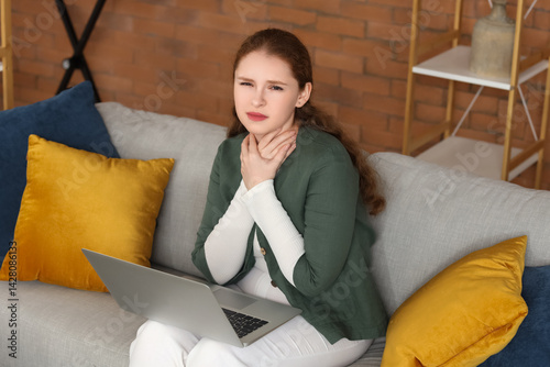 Sick young woman with sore throat and laptop sitting on sofa at home