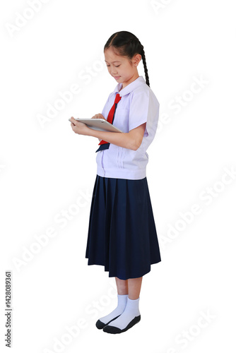 Asian schoolgirl in school uniform bow her head intently playing tablet computer while standing isolated on white background. Full body photo with clipping path.