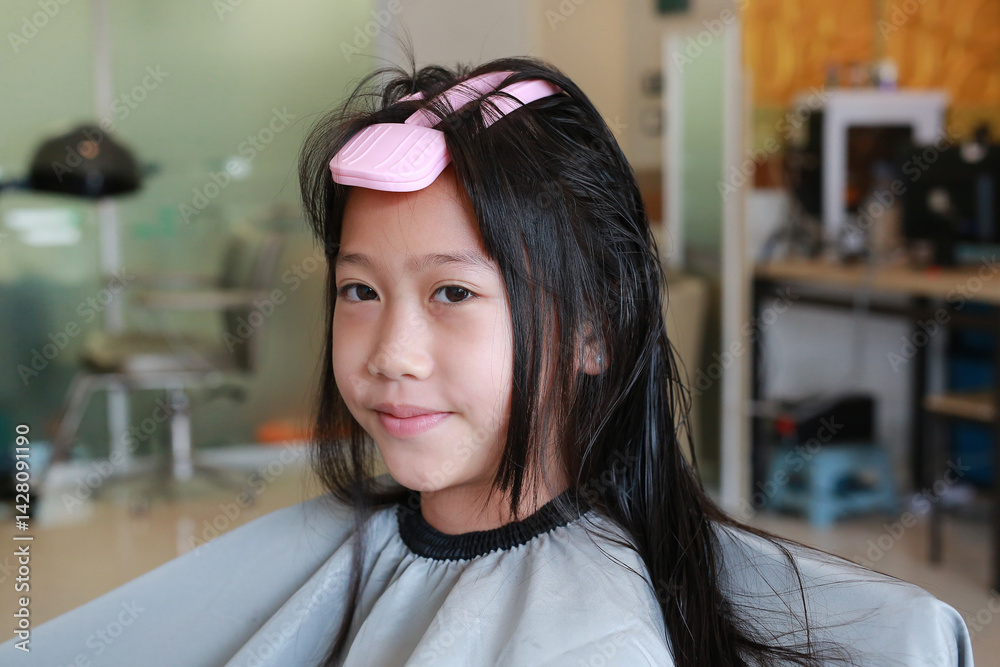 Portrait of Asian girl child getting her haircut in a beauty salon. Close up.