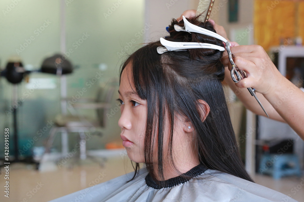 Asian girl having her hair cut by beautician in beauty salon.