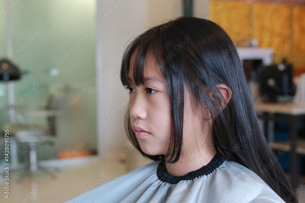 Asian girl having her hair cut by beautician in beauty salon.