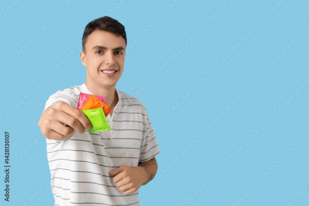 Young man showing condoms on blue background Young man showing condoms on blue background