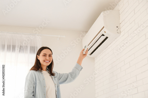 Pretty young woman using air conditioner remote control at home