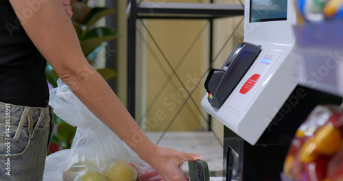 Customer pays at self-checkout using smartphone next to grocery bag photo