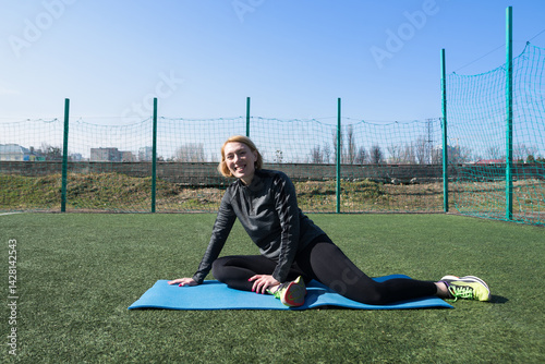 Athletic woman doing exercises on fitness mat outdoors at city stadium.