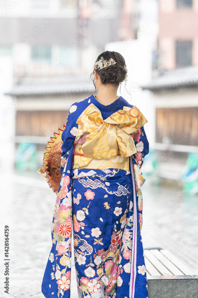 It's a rainy summer day. bus stop. A Japanese woman in a teenager wearing a blue kimono folding a Japanese umbrella.
