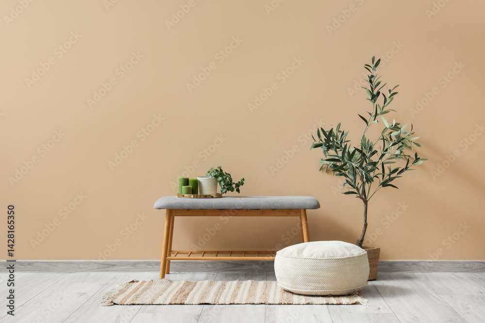 Bench with candles and houseplant, decorative tree and pouf near beige wall in room