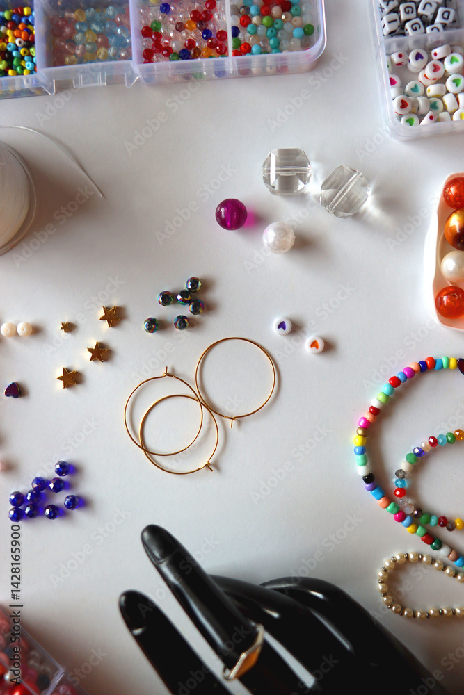 Hand figurine, colorful friendship bracelets, necklaces, various beads and DIY supplies on the table. Making jewelry at home. Flat lay.