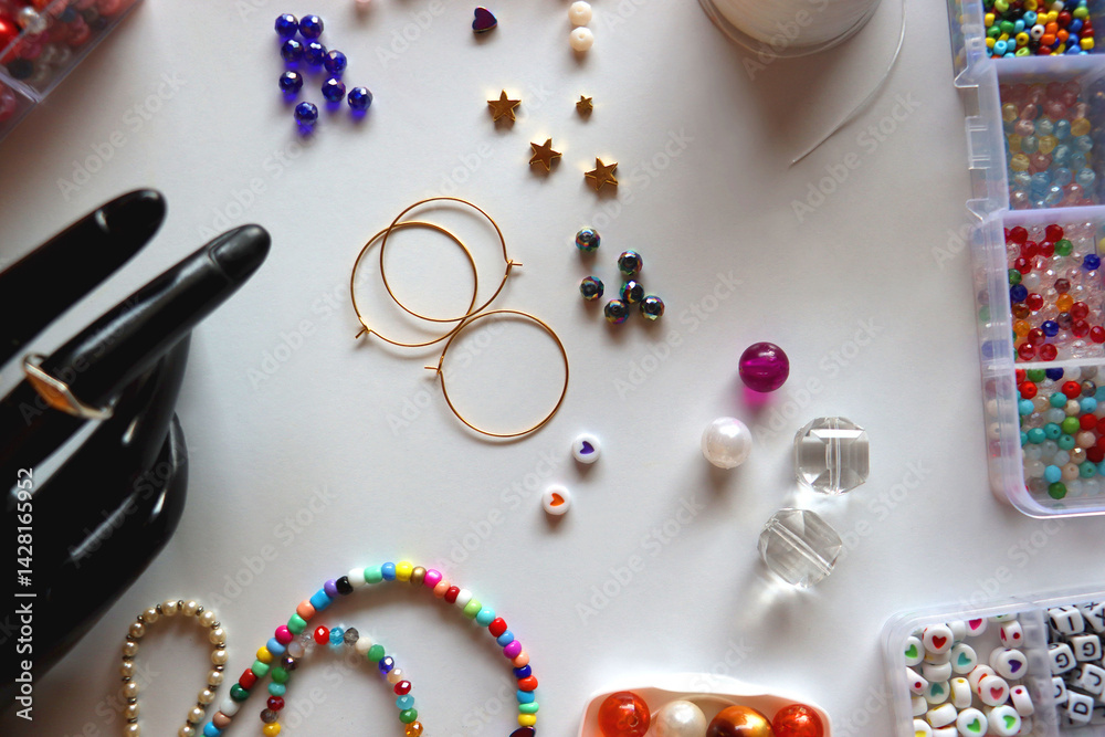 Hand figurine, colorful friendship bracelets, necklaces, various beads and DIY supplies on the table. Making jewelry at home. Flat lay.