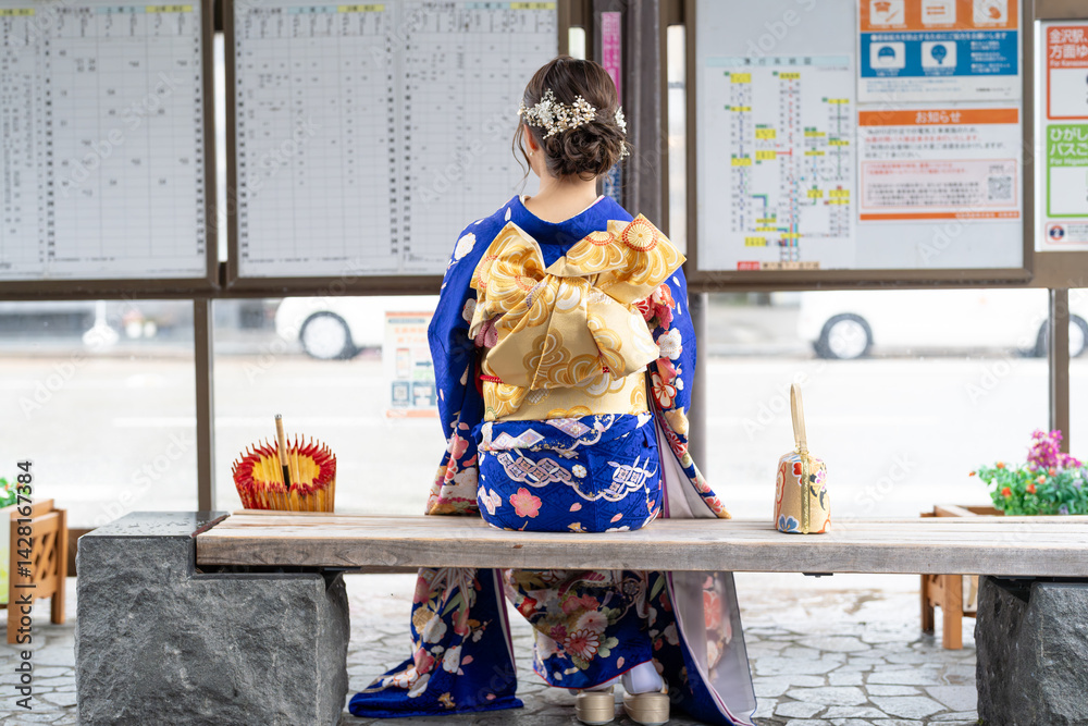 It's a rainy summer day. bus stop. A Japanese woman in a teenager wearing a blue kimono folded and placed it by her side, sitting on a bench.