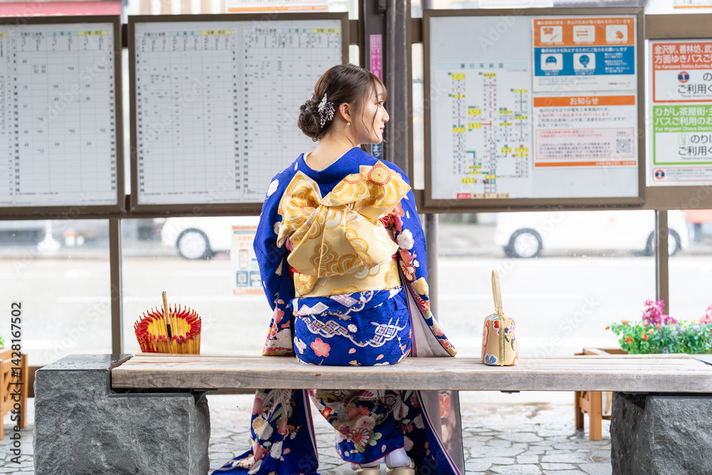 It's a rainy summer day. bus stop. A Japanese woman in a teenager wearing a blue kimono folded and placed it by her side, sitting on a bench.