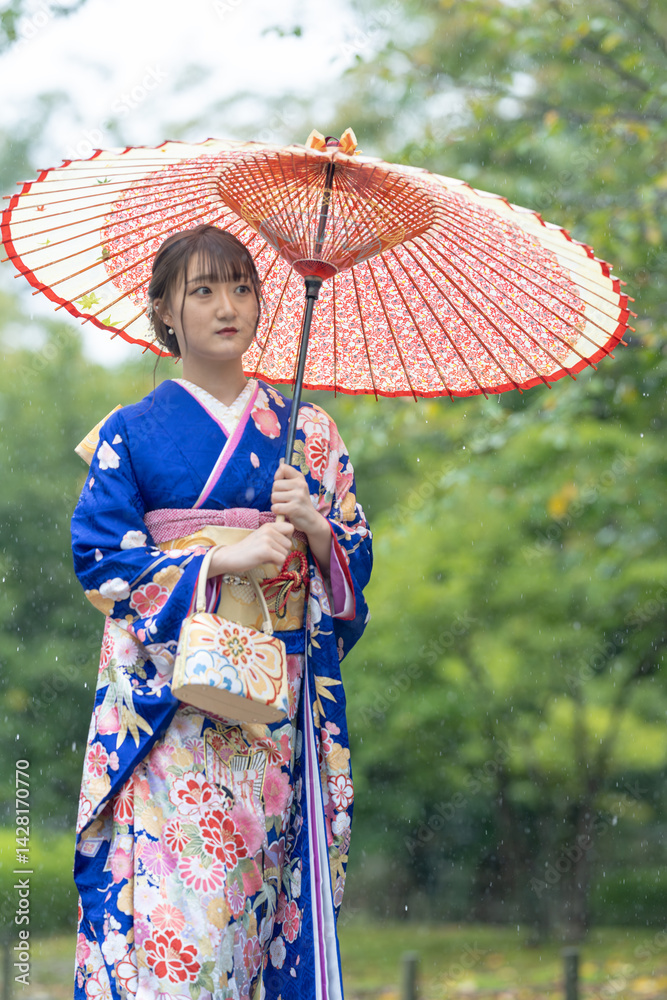 A local city in Japan on a rainy summer day. Japanese woman wearing a blue kimono for teenagers with a Japanese umbrella walking through a traditional garden.