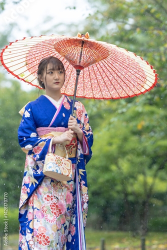 Obraz na płótnie A local city in Japan on a rainy summer day. Japanese woman wearing a blue kimono for teenagers with a Japanese umbrella walking through a traditional garden. w salonie