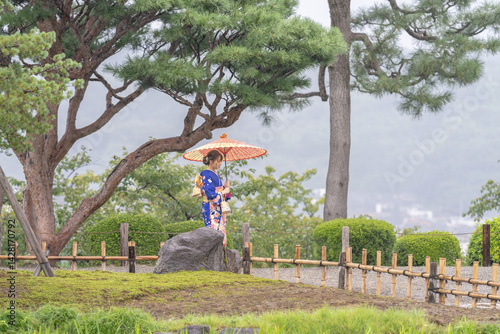 Obraz na płótnie A local city in Japan on a rainy summer day. Japanese woman wearing a blue kimono for teenagers with a Japanese umbrella walking through a traditional garden. w salonie