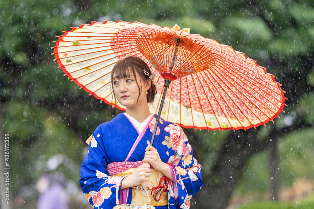 A local city in Japan on a rainy summer day. Japanese woman wearing a blue teenage kimono with a Japanese umbrella walking along a traditional garden bridge.