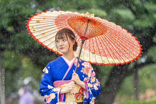 Obraz na płótnie A local city in Japan on a rainy summer day. Japanese woman wearing a blue teenage kimono with a Japanese umbrella walking along a traditional garden bridge. w salonie