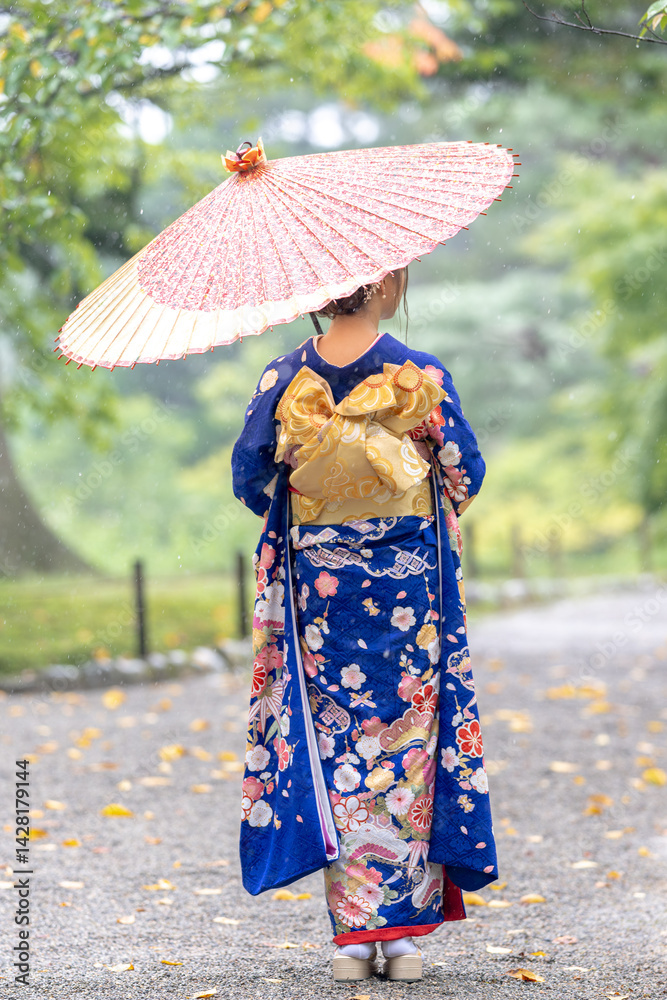A local city in Japan on a rainy summer day. Japanese woman wearing a blue kimono for teenagers with a Japanese umbrella walking through a traditional garden.
