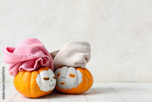 Pumpkins with drawn faces, clay masks and towels on tile table near light wall