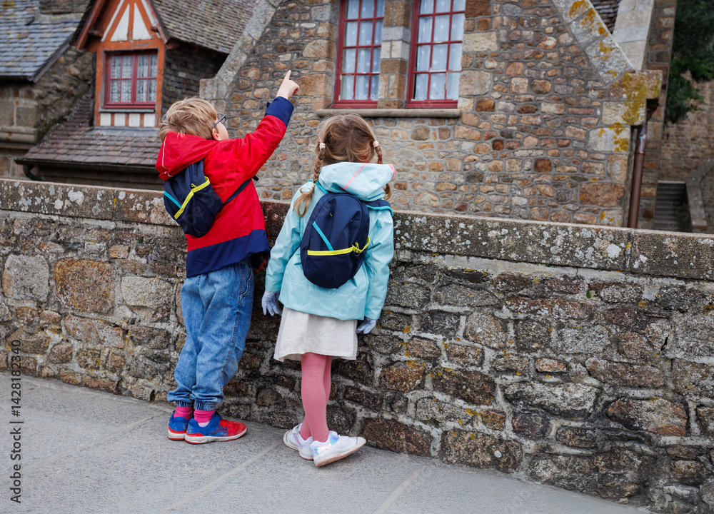 Children pointing at a historic stone house, wearing backpacks